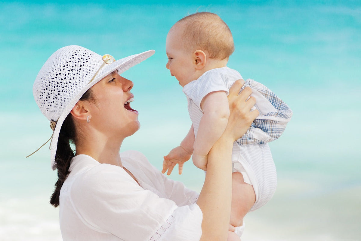 Happy mother lifting her baby into the air at the beach