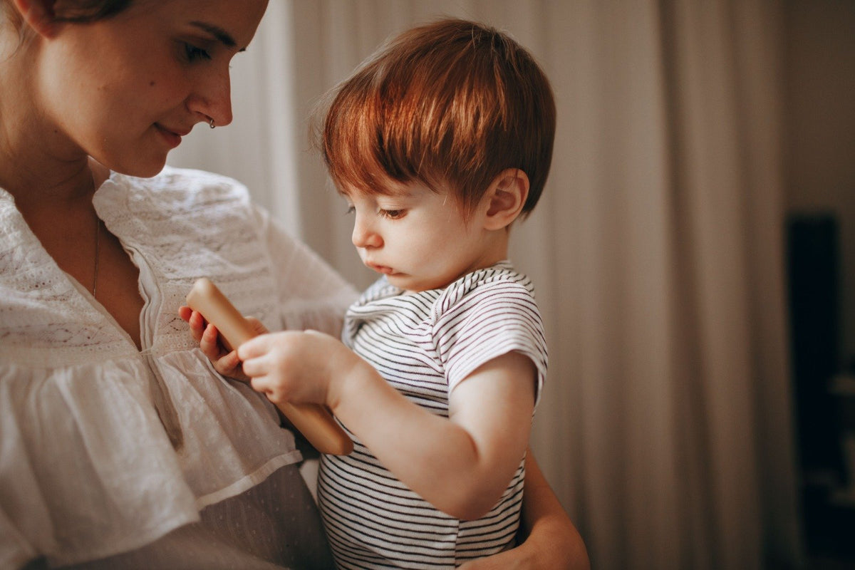 Mother watching her young son explore a wooden toy