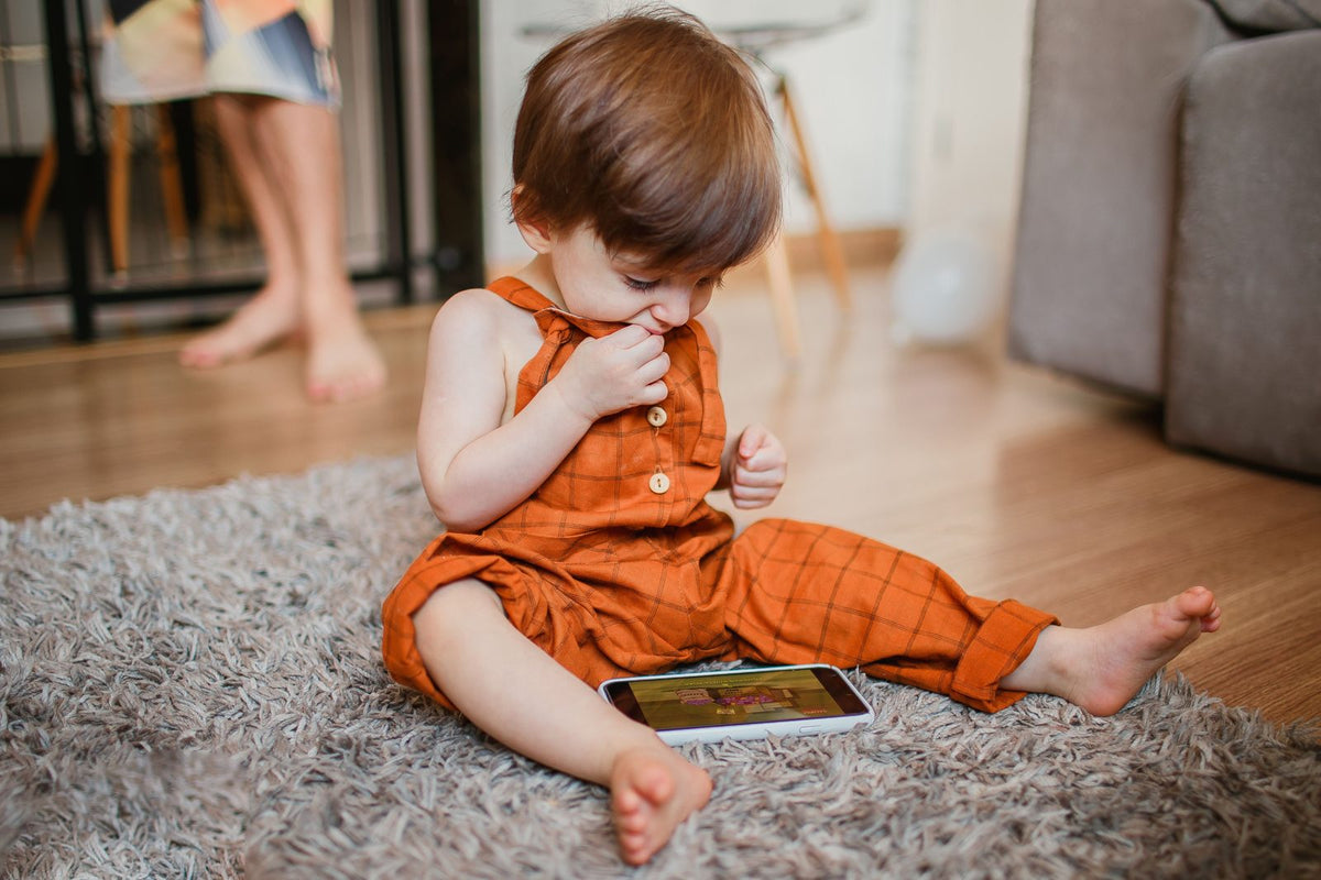 Toddler sitting on a rug looking at a smartphone