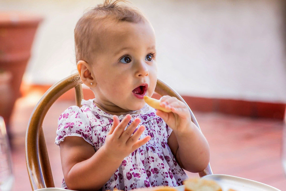 Toddler girl in a high chair tasting a new food